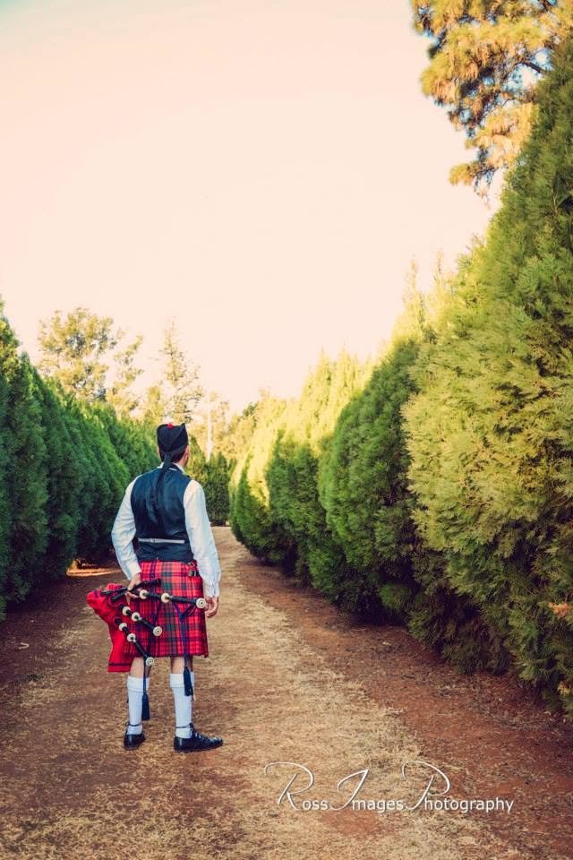 Piper Paul standing with bagpipes on a garden path